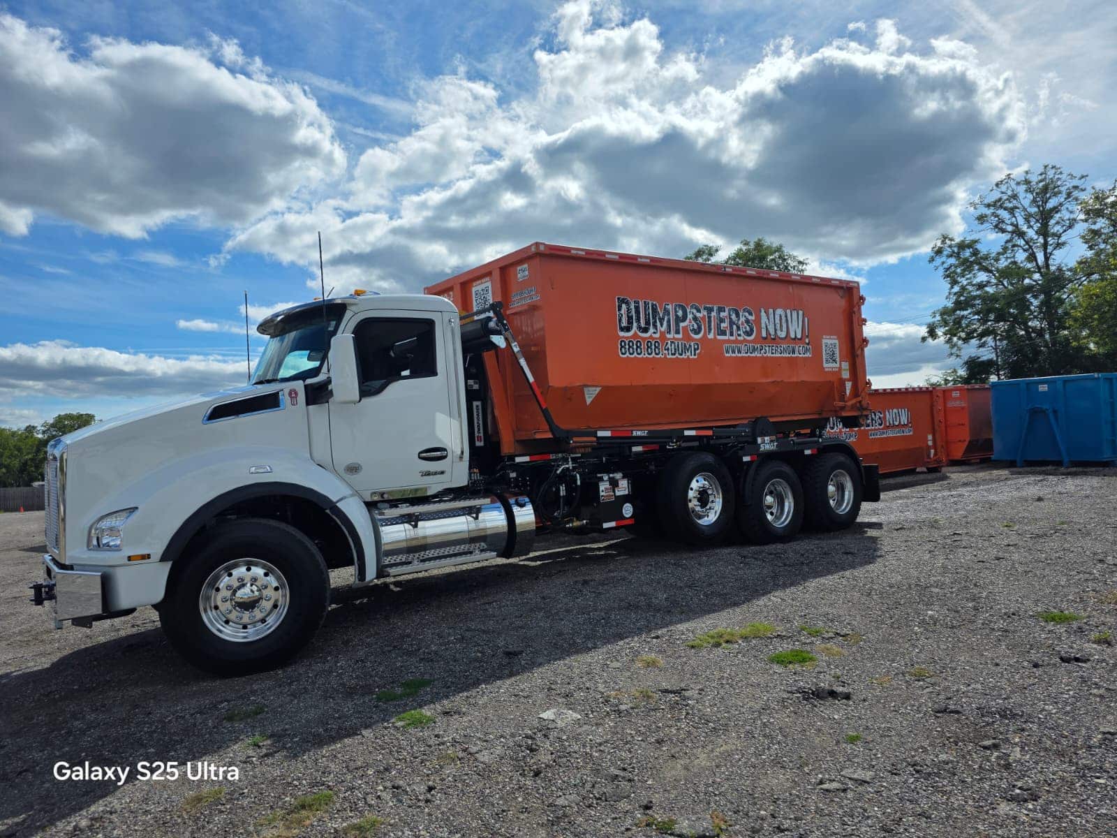 White truck with orange dumpster parked on gravel lot.